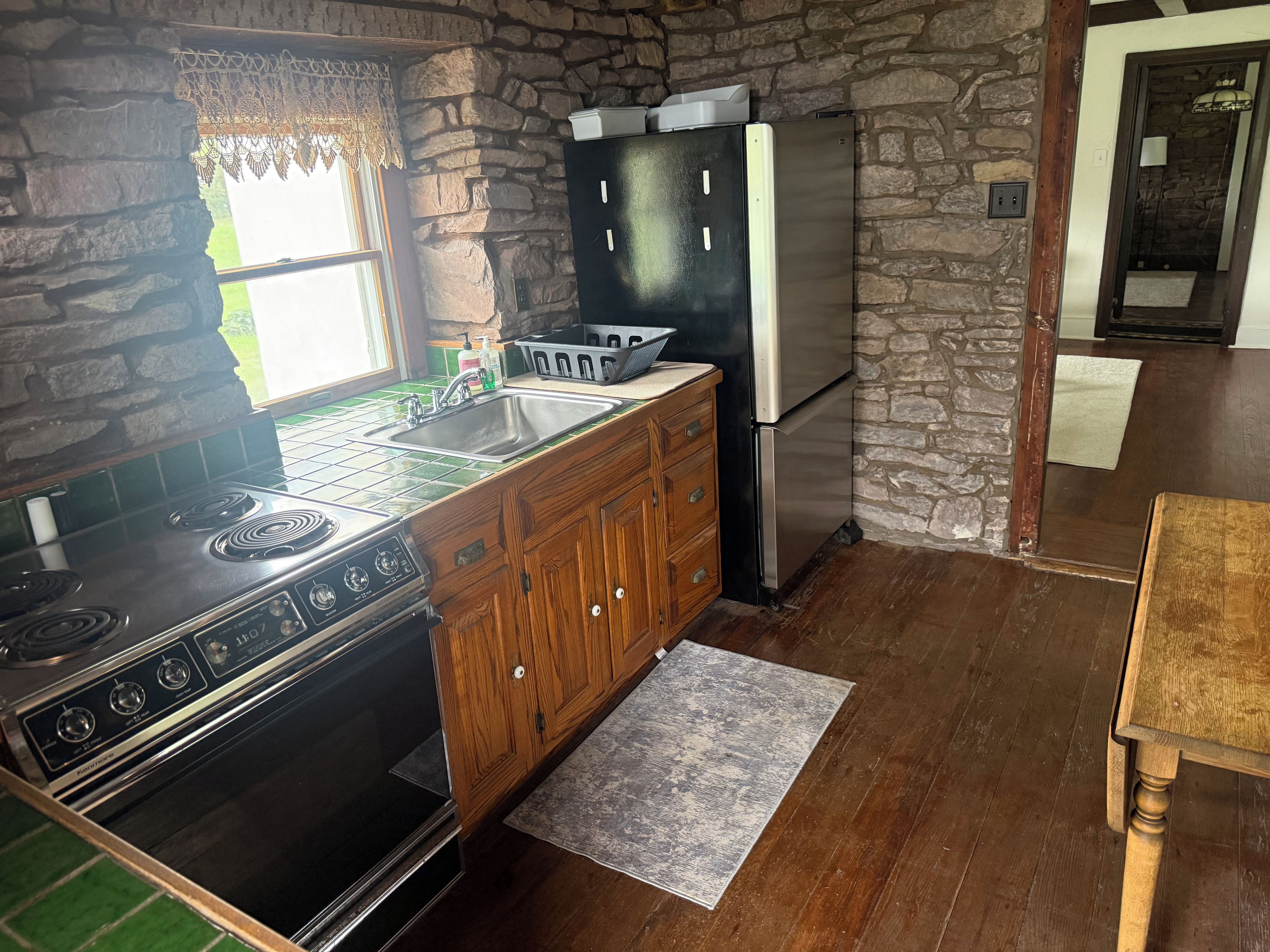 A kitchen with a stone wall, a stove, a refrigerator, and wooden cabinets.