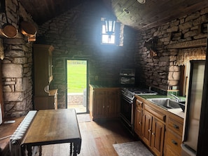 Una cocina rústica con paredes de piedra, armarios de madera, horno empotrado y ventana con vistas a un área cubierta de césped.