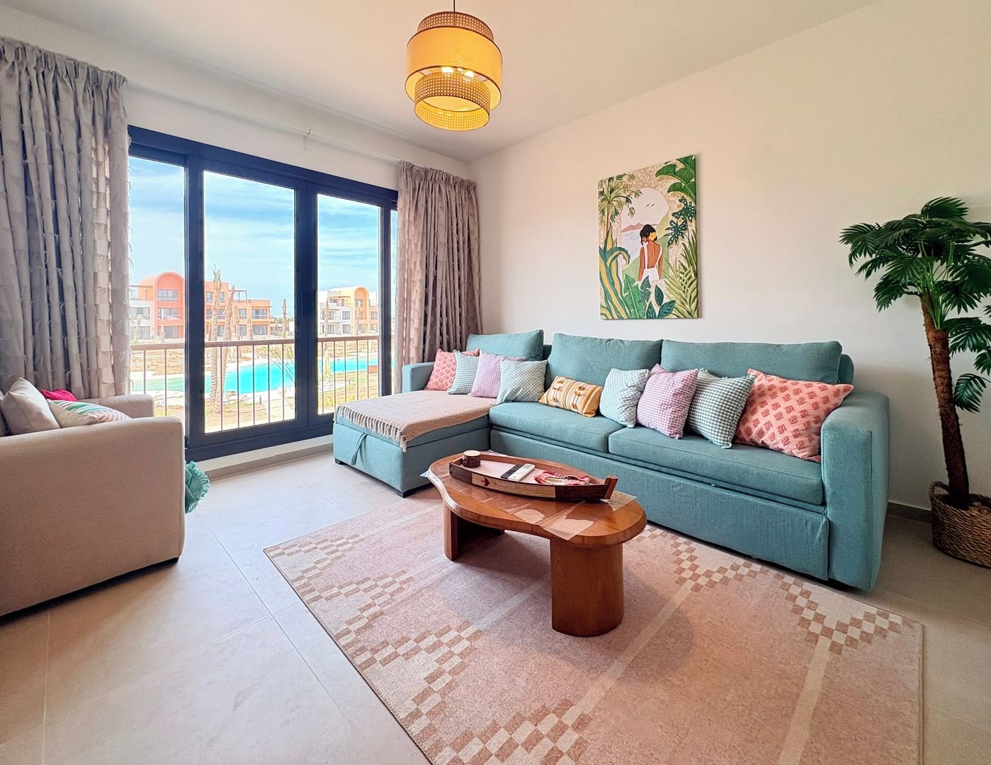 A spacious living room with a large window, a sofa set, a coffee table, and a potted plant.