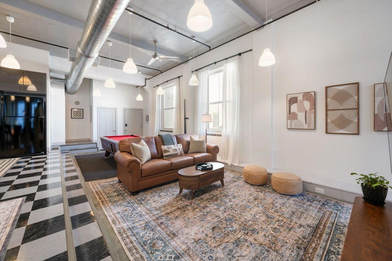 A modern living room with a pool table, leather sofa, and a patterned rug.