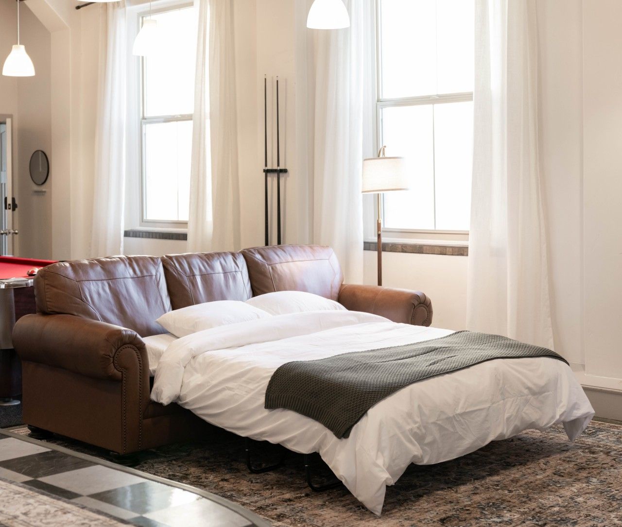 A bedroom with a large bed, a brown leather sofa, a red pool table, and a lamp.