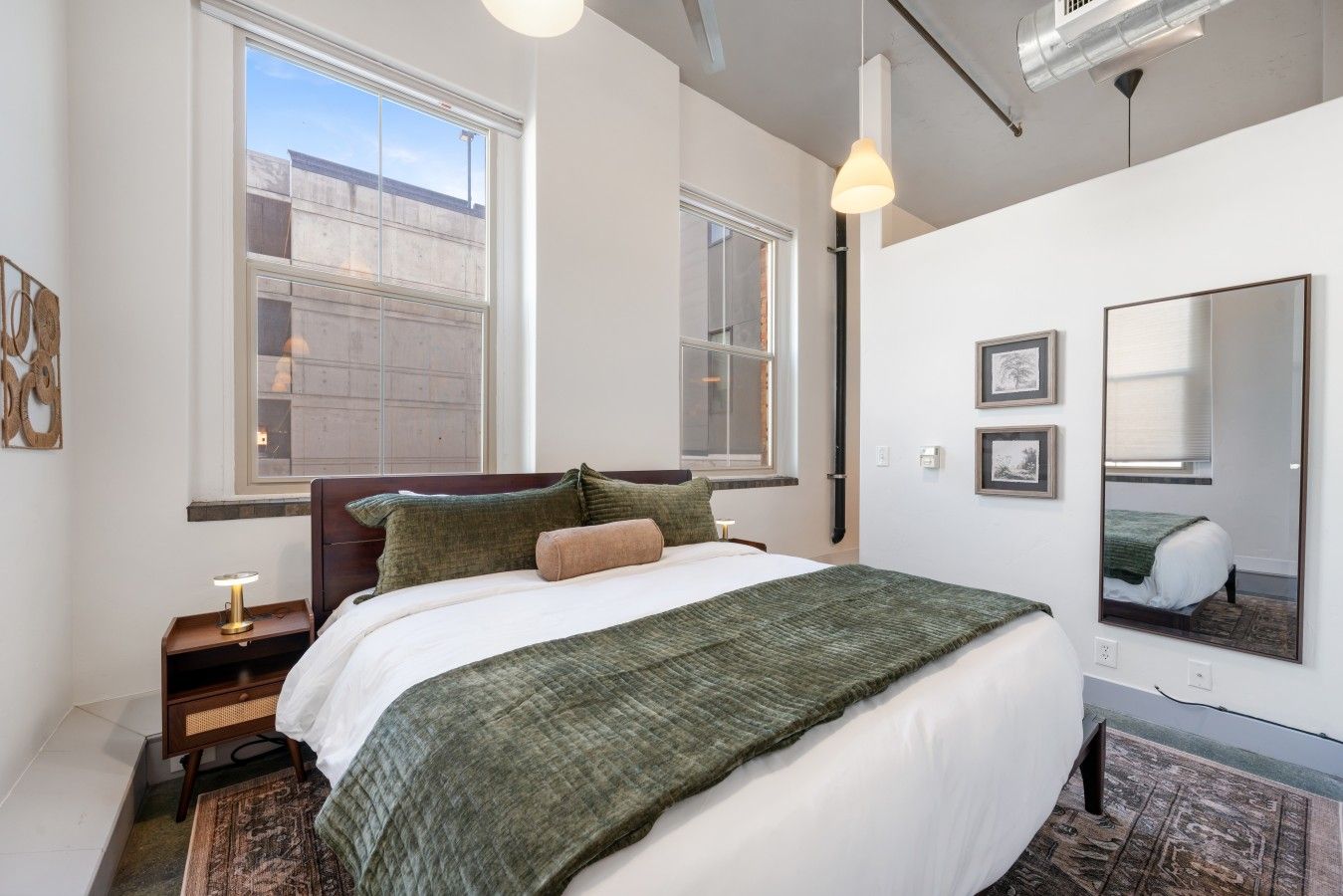 A hotel room with a bed, bedside table, lamp, and a large window.