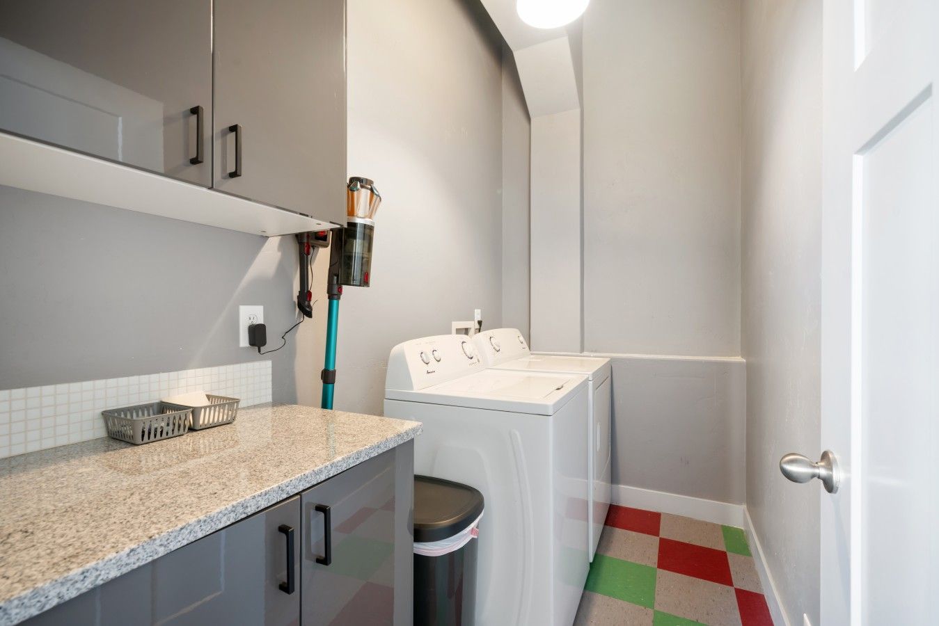 A laundry area with a washing machine, a drying machine, a trash bin, and a countertop with a basket.