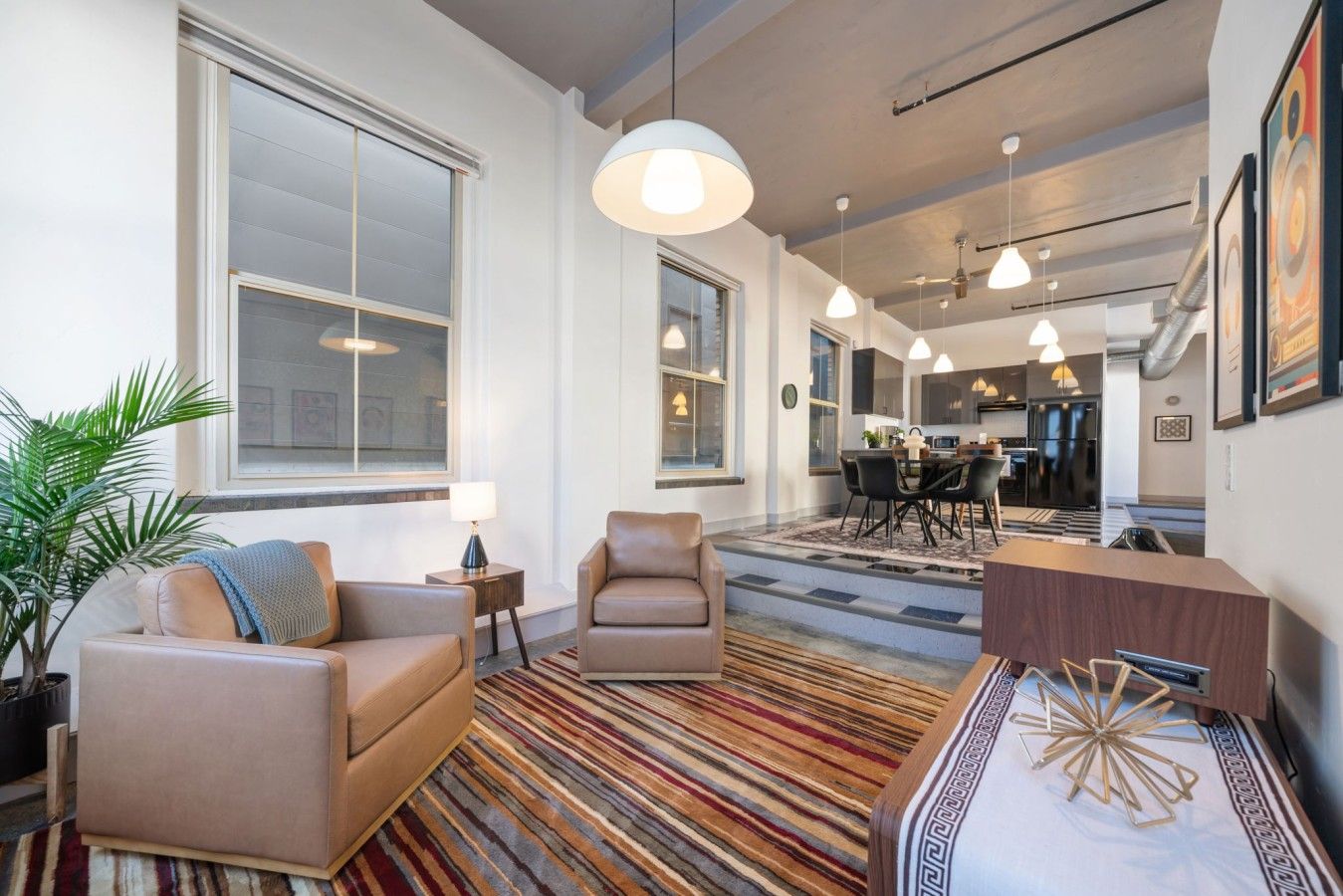 Una sala moderna con un sofá, un sillón y una mesa de centro. Hay una zona de comedor con una mesa y sillas, y una cocina al fondo.