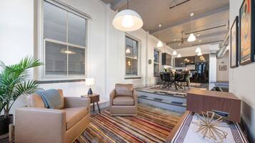 Una sala moderna con un sofá, un sillón y una mesa de centro. Hay una zona de comedor con una mesa y sillas, y una cocina al fondo.