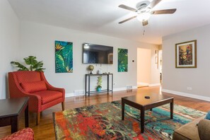 A living room with a red armchair, a coffee table, a colorful rug, a flat-screen TV, and artwork on the walls.
