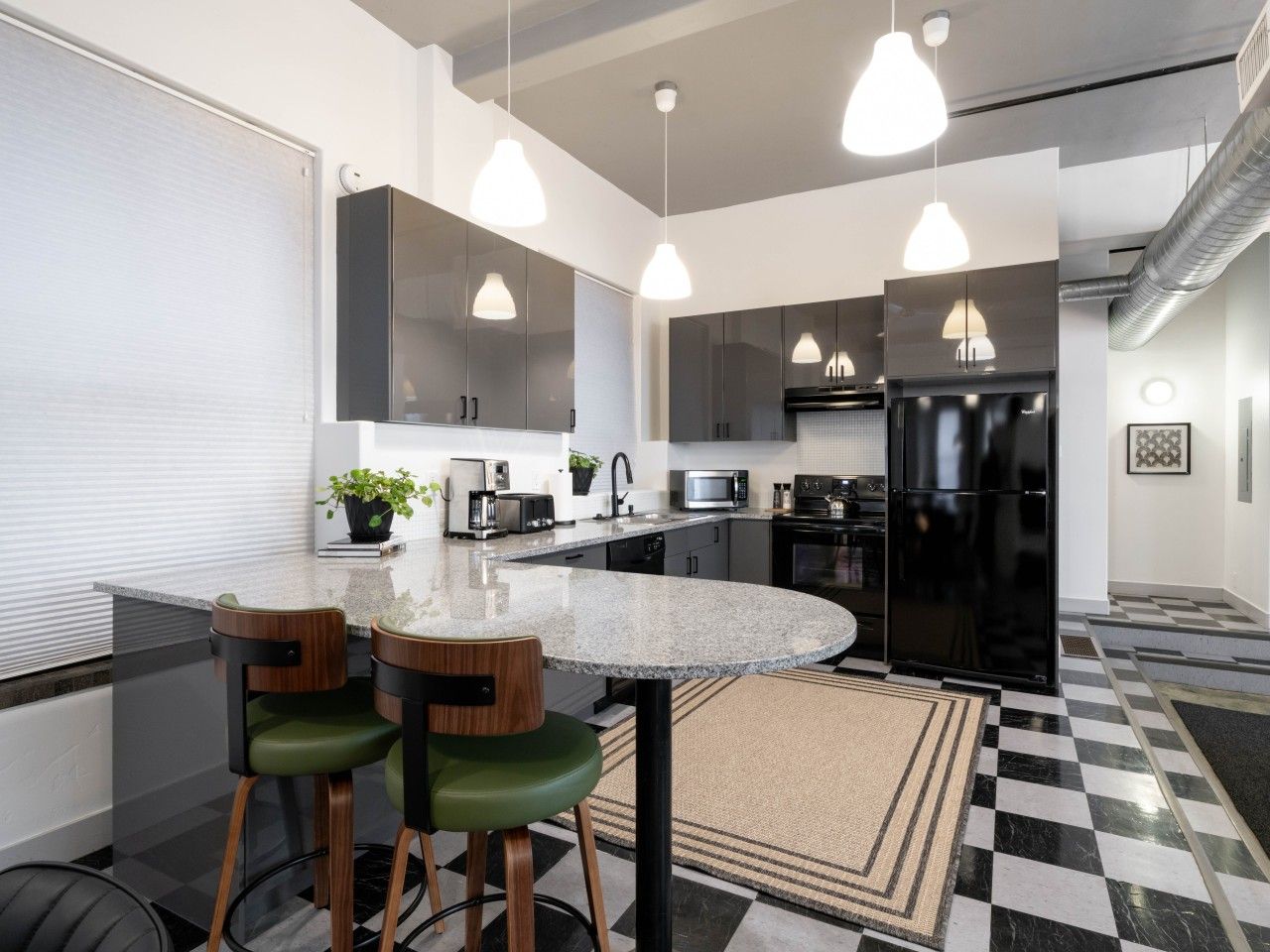 A modern kitchen with a central island, pendant lighting, and a checkered floor pattern.