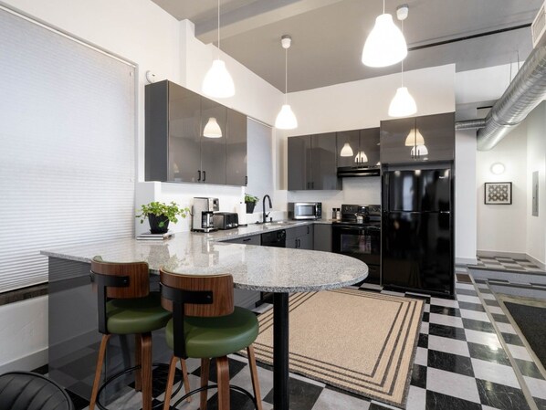 A modern kitchen with a central island, pendant lighting, and a checkered floor pattern. - Central Downtown Gem | Perfect for BYU Games! (Provo)