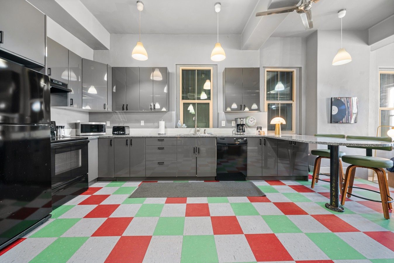 Uma cozinha moderna com armários cinza, uma geladeira preta e um chão colorido em xadrez.