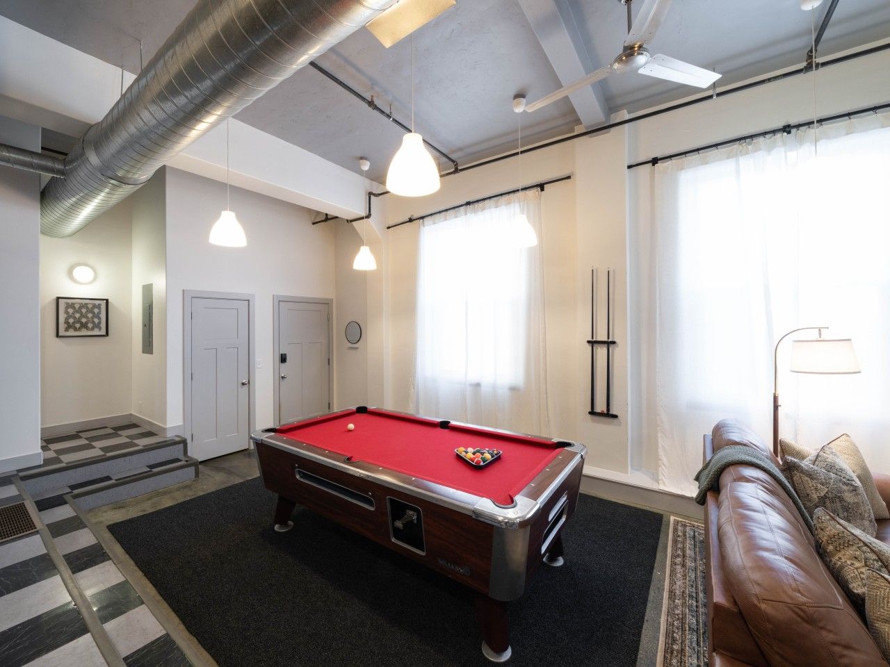 Een pooltafel in een ruimte met een geruit vloerkleed, een bank en een lamp.