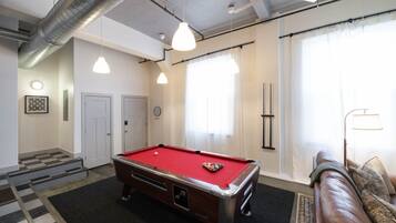 Een pooltafel in een ruimte met een geruit vloerkleed, een bank en een lamp.