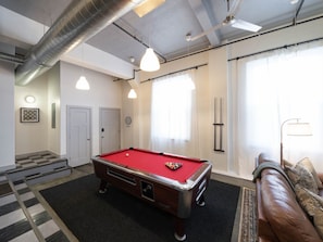 Een pooltafel in een ruimte met een geruit vloerkleed, een bank en een lamp.