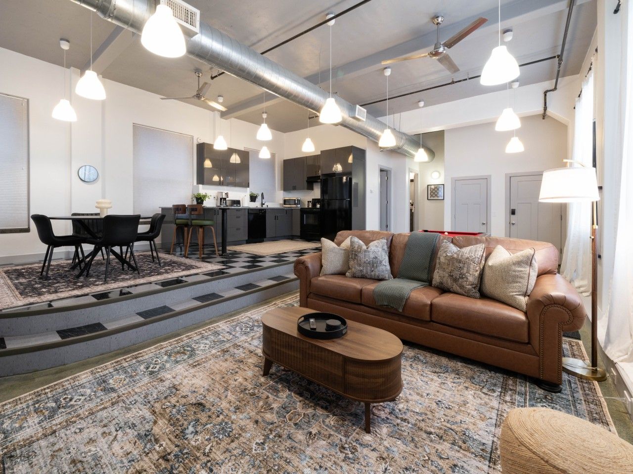 A spacious living area with a brown leather sofa, a coffee table, and hanging pendant lights.