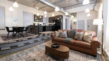 A spacious living area with a brown leather sofa, a coffee table, and hanging pendant lights.
