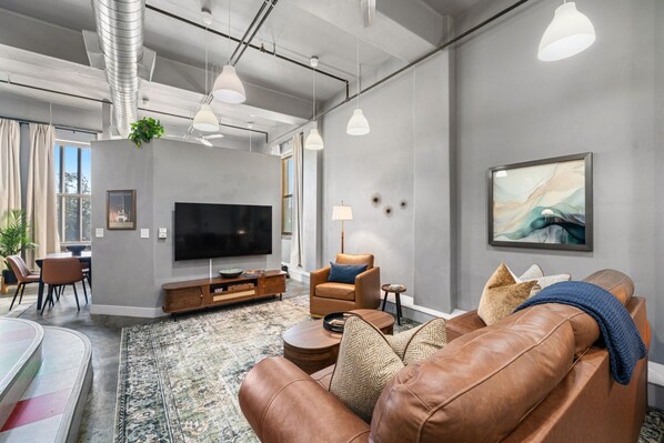 A modern living room with a leather sofa, a flat-screen TV, and a dining area with a table and chairs.