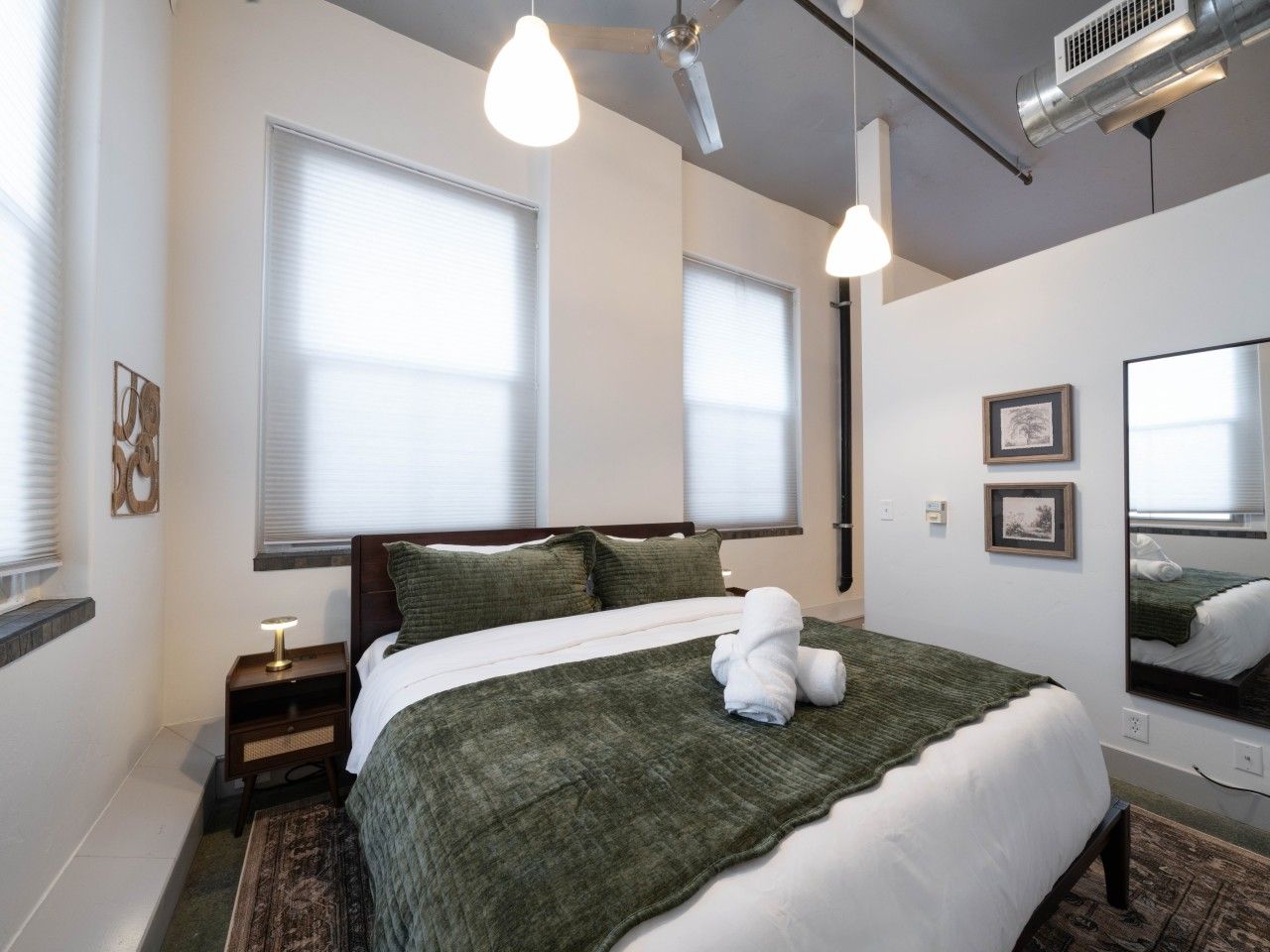 A bedroom with a bed, bedside tables, a mirror, and a window with blinds.
