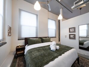 A bedroom with a bed, bedside tables, a mirror, and a window with blinds. - Central Downtown Gem | Perfect for BYU Games! (Provo)