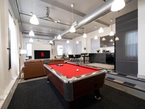 A pool table in a modern room with a sofa, a television displaying the Netflix logo, and a kitchen area. - Central Downtown Gem | Perfect for BYU Games! (Provo)