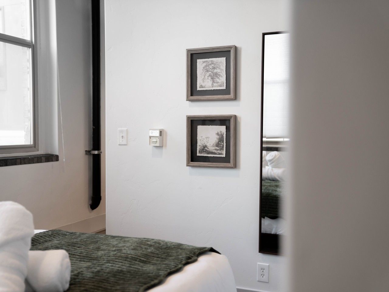 A bedroom with a bed, a wall-mounted mirror, and two framed pictures.