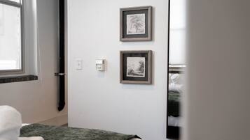 A bedroom with a bed, a wall-mounted mirror, and two framed pictures.