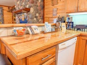 A kitchen with wooden cabinets, a stone wall, and various items on the counter including a coffee maker, a dish rack, and packaged food.