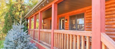 A log cabin with a covered porch, a small tree, and a window with a view.