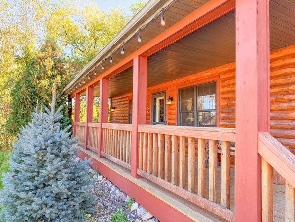 A log cabin with a covered porch, a small tree, and a window with a view.