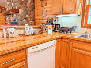Una cocina con armarios de madera, pared de piedra, cafetera y lavavajillas.