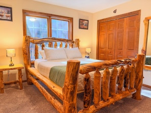 A bedroom with a wooden bed frame, two bedside tables, a large window, and a wooden wardrobe.