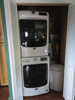 A compact laundry room with a stacked washer and dryer, a water heater, and a toilet.