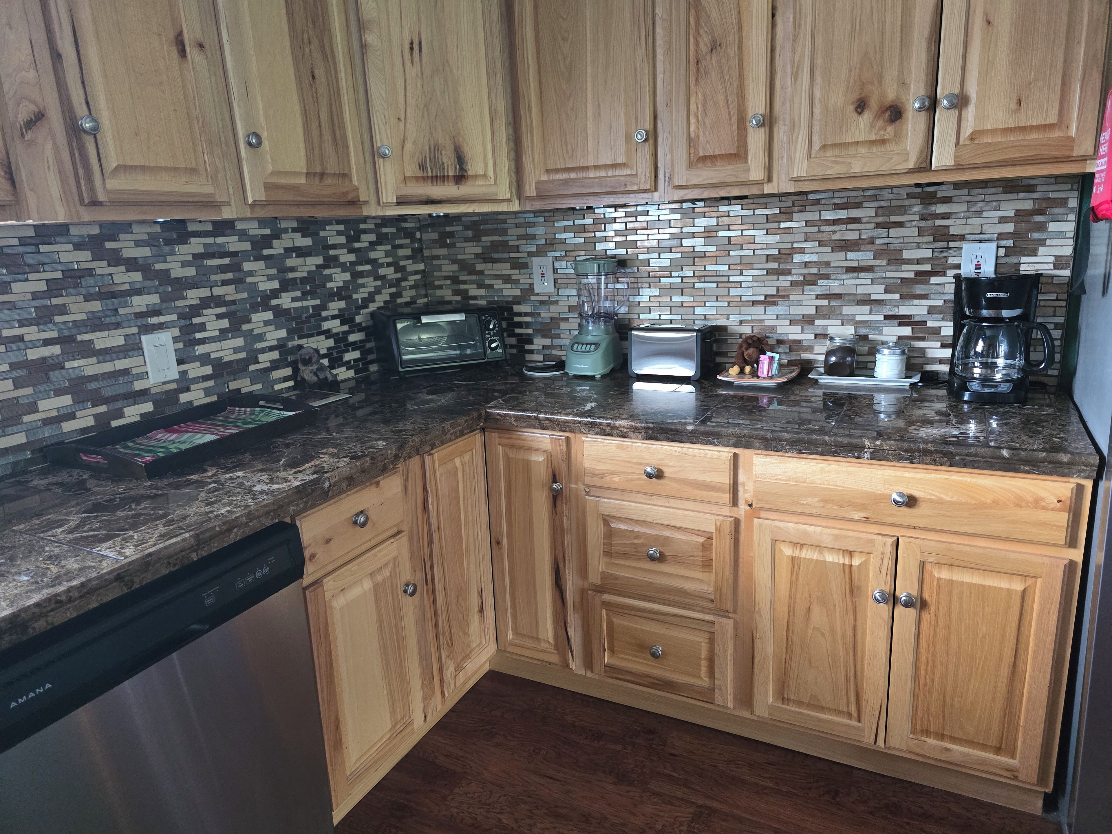 Una cocina con armarios de madera, salpicadero de azulejos y varios electrodomésticos, incluyendo microondas, tostadora y cafetera.