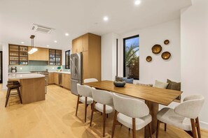 Eine moderne Küche mit einer zentralen Kochinsel, Edelstahlgeräten und einem Essbereich mit einem Holztisch und Stühlen.