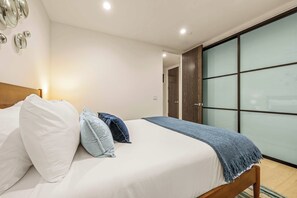 A modern bedroom with a bed, pillows, a blanket, and a sliding glass door leading to a bathroom. - 5BR | Hot Tub | Walk to Beach | Family House (San Diego)