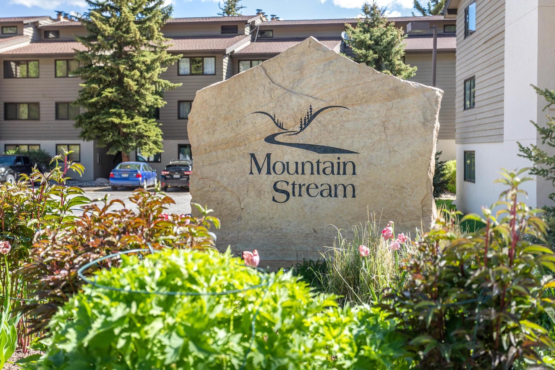 A stone sign with the text 'Mountain Stream' and a mountain design, surrounded by greenery.