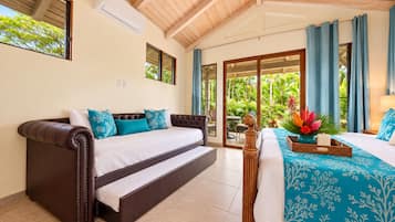 A bedroom with a sofa bed, a separate bed, a window with curtains, and a view of greenery outside.