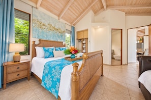 A bedroom with a wooden bed, a nightstand, a window with curtains, and a bathroom visible through an open door. - NEW 1 ACRE POIPU ESTATE - Sleeps 32 - Full AC - 8 Ensuites - Poipu Beach Club (Koloa)