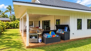 A covered outdoor area with a grill, seating, and storage bins. - NEW 1 ACRE POIPU ESTATE - Sleeps 32 - Full AC - 8 Ensuites - Poipu Beach Club (Koloa)