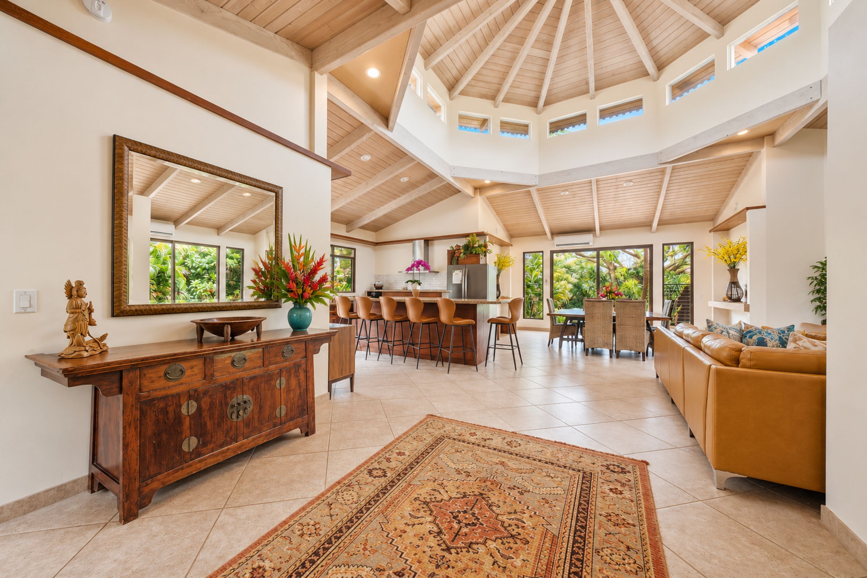 A spacious living area with a high ceiling, a large mirror, a wooden cabinet, a sofa, and a dining area with chairs and a table.