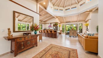 A spacious living area with a high ceiling, a large mirror, a wooden cabinet, a sofa, and a dining area with chairs and a table.