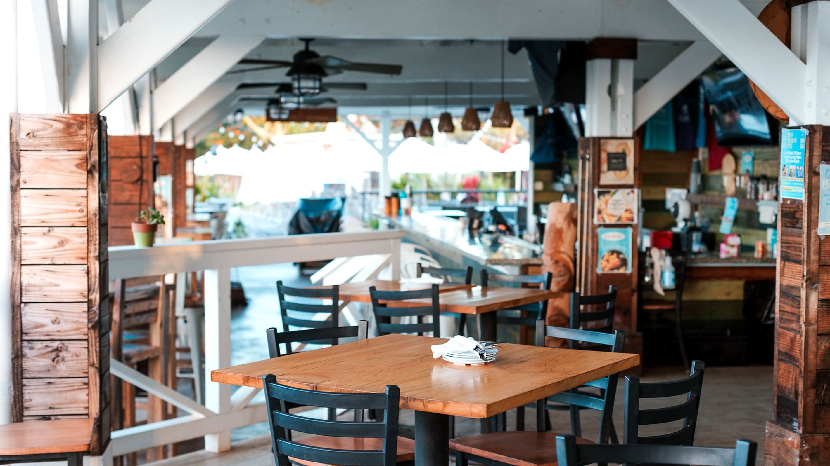 Un espace de restauration intérieur avec des tables et des chaises en bois, un comptoir avec des panneaux affichant le menu, et une vue sur l’extérieur.
