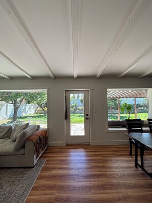 Ein geräumiges Wohnzimmer mit Holzboden, einer Couch, einem Esstisch und einem großen Fenster.