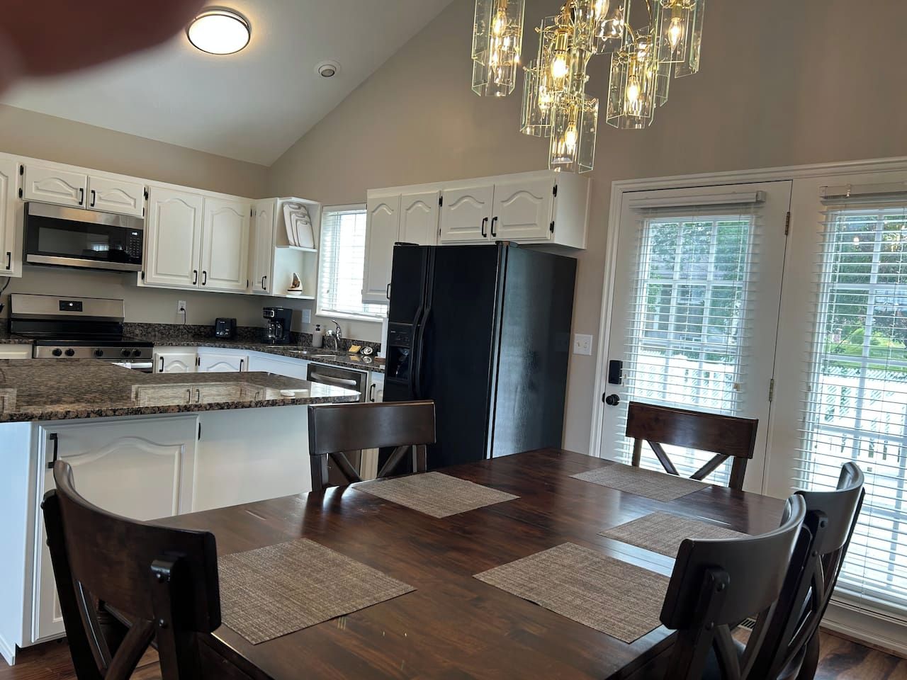 A kitchen with white cabinets, a black refrigerator, a dining table with chairs, and a chandelier.