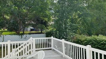 A wooden deck with white railings, surrounded by lush greenery and trees.