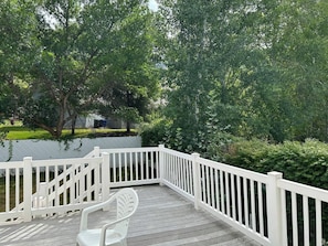 Une terrasse en bois avec des rampes blanches, entourée d’une végétation luxuriante et d’arbres.