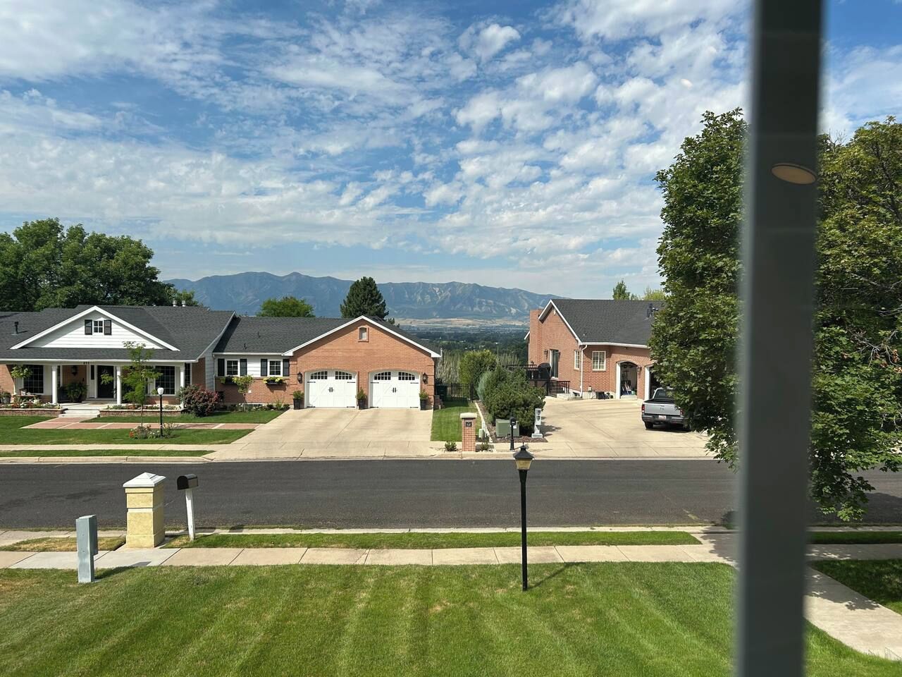 A suburban street with two brick houses, a clear sky, and mountains in the background.