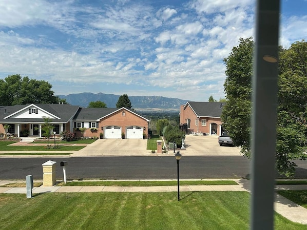 Una calle residencial con dos casas de ladrillo, cielo despejado y montañas al fondo.