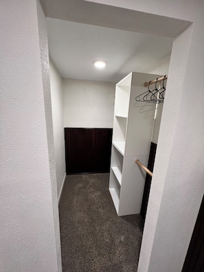 Ein schmaler Flur mit einer weißen Wand, einer dunkelholzigen Verkleidung und einer weißen Regaleinheit mit einem Holzgriff.
