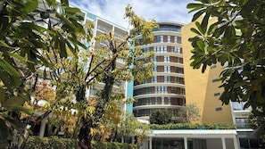 Um edifício com vários andares e varandas, cercado por vegetação exuberante e árvores.
