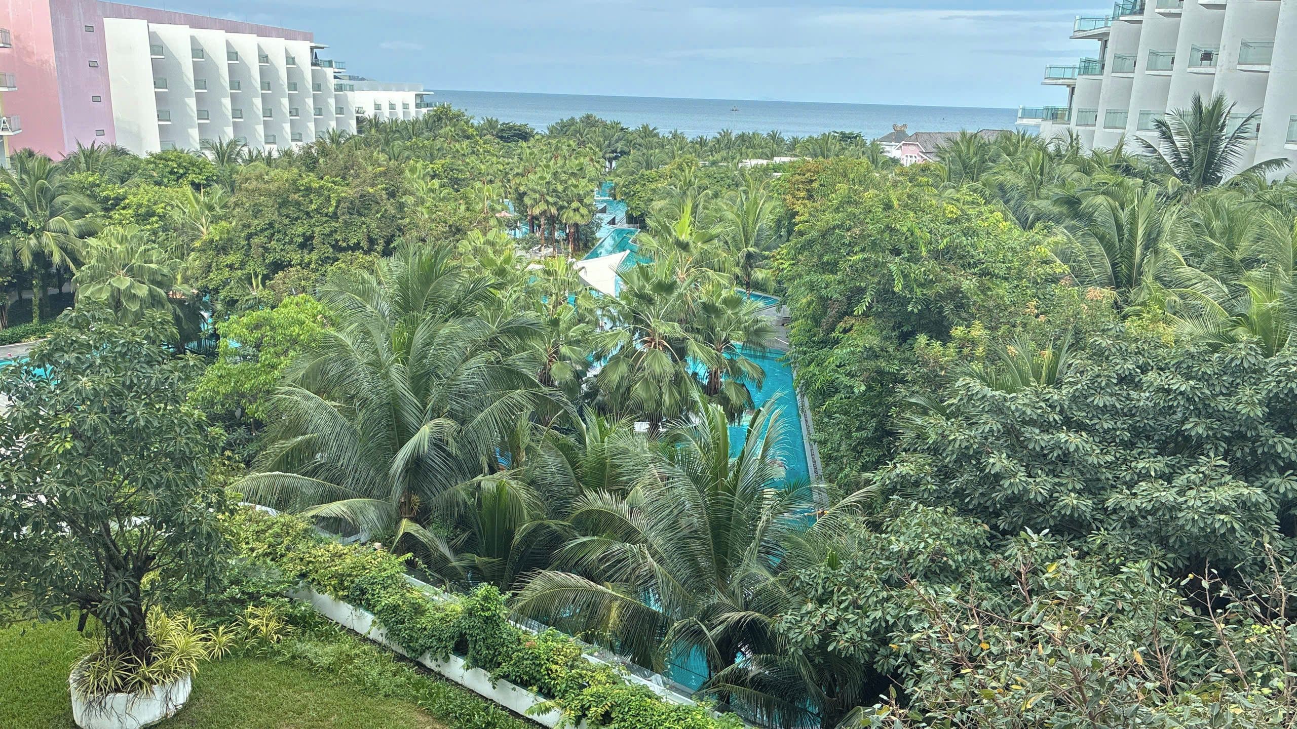 Un resort con piscina rodeada de exuberante vegetación tropical y edificios modernos al fondo.