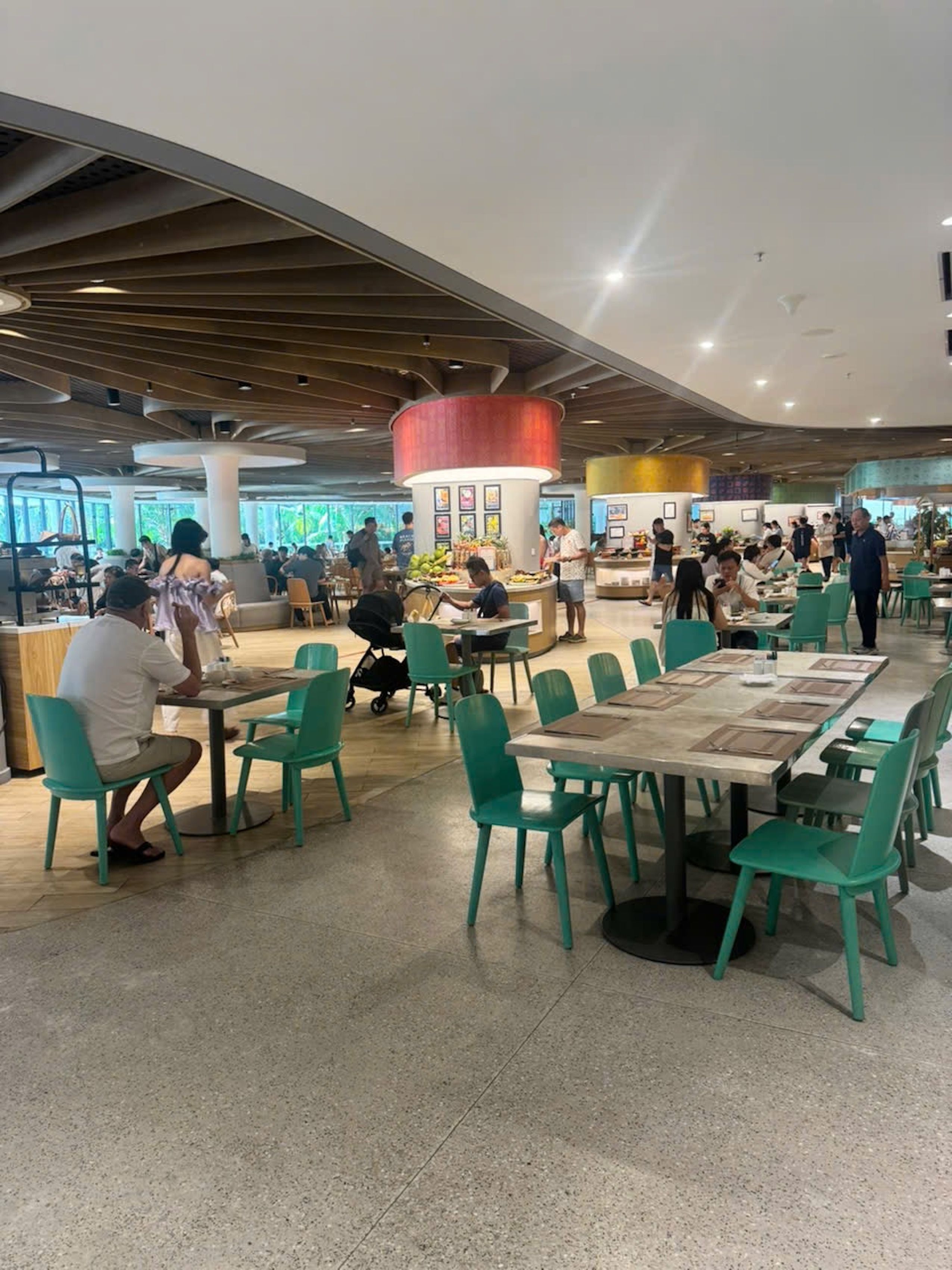 A spacious indoor dining area with multiple tables and chairs, a central serving station, and a modern ceiling design.